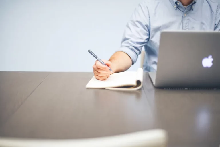 Uomo che prende appunti su un quaderno accanto al portatile, il momento della scelta fra le edizioni Zoho