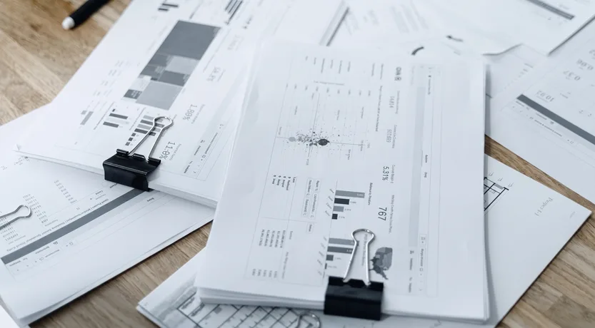 Fogli stampati con tabelle e grafici accatastati sulla scrivania, i dati da portare da Excel al CRM