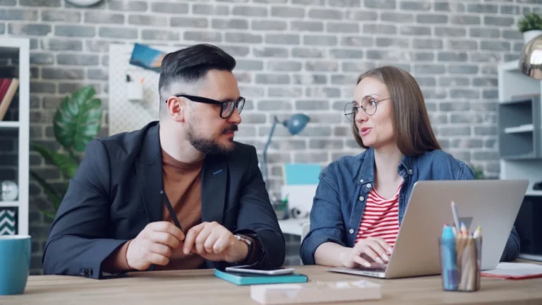 Due colleghi alla scrivania commentano insieme i numeri sullo schermo di un laptop in un ufficio
