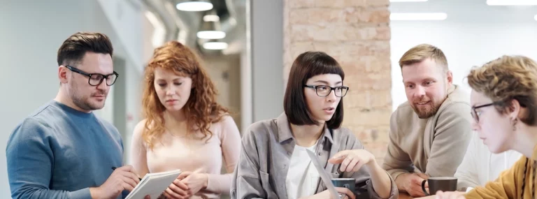 Colleghi di reparti diversi discutono attorno a un laptop in ufficio, condividendo gli stessi dati sul cliente