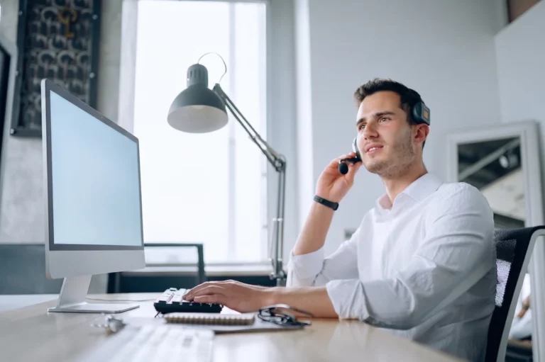 Operatore con cuffie e microfono risponde a un cliente davanti al computer, in un ufficio luminoso