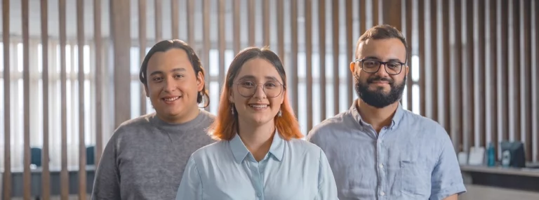 Tre colleghi sorridenti in un ufficio con pareti a doghe di legno, le persone che usano ogni giorno gli strumenti aziendali