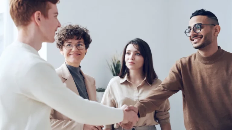 Stretta di mano fra un nuovo collega e il team in un ufficio luminoso, il momento dell'ingresso in azienda