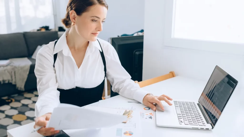 Donna alla scrivania legge un report stampato accanto a un portatile