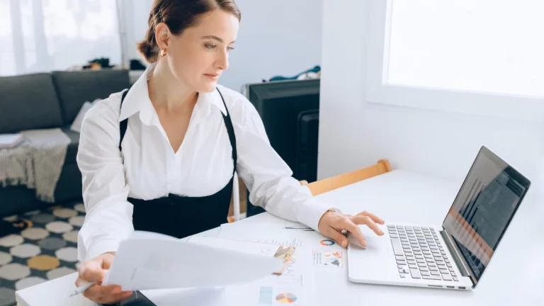 Donna alla scrivania legge un report stampato accanto a un portatile